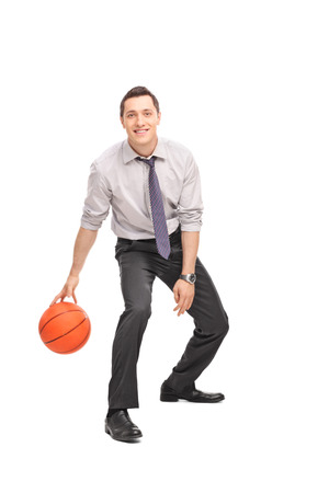 Full length portrait of a cheerful young businessman playing basketball and looking at the camera isolated on white backgroundの写真素材