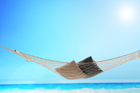 An empty hammock with a couple of pillows on it shot on a beach by the oceanの写真素材