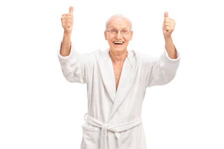 Studio shot of an overjoyed senior in a white bathrobe giving two thumbs up and looking at the camera isolated on white backgroundの写真素材
