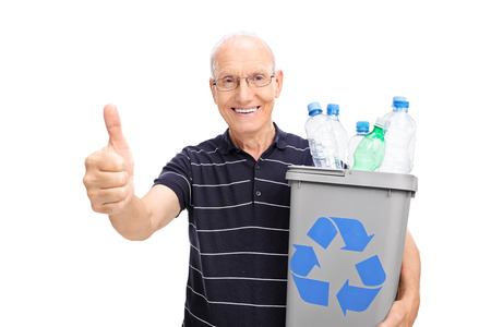 Cheerful senior holding a recycle bin full of plastic bottles and giving a thumb up isolated on white backgroundの写真素材
