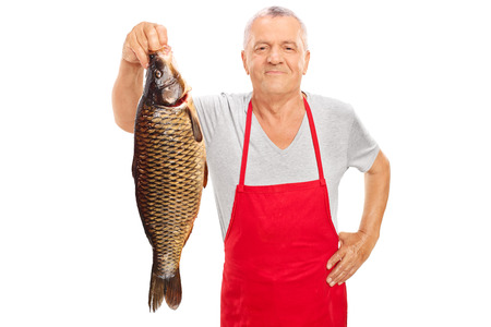 Mature fishmonger in a red apron holding a large freshwater fish and looking at the camera isolated...