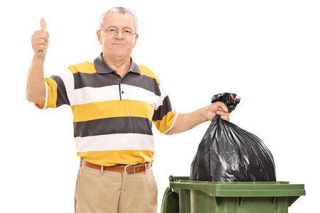 Senior giving a thumb up by a trash can isolated on white backgroundの写真素材