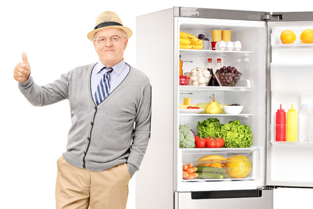 Senior leaning on a fridge and giving thumb up isolated on whiteの写真素材