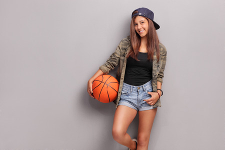 Cool teenage girl holding a basketball and leaning against a gray wall Cool teenage girl holding a basketball and leaning against a gray wall