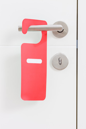 Close-up on a metal handle of a white door with a red do not disturb label on itの写真素材