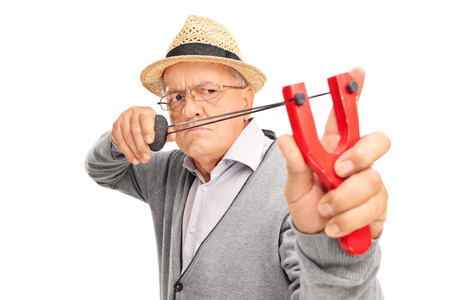 Angry senior gentleman aiming to shoot a rock with a slingshot isolated on white backgroundの写真素材