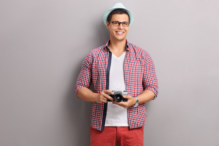 Young male photographer holding a camera and posing in front of a gray wallの写真素材