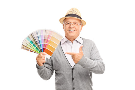 Senior gentleman holding a color palette guide in one hand and pointing towards it with the other isolated on white backgroundの写真素材