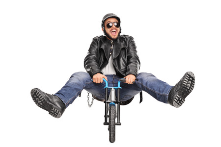 Studio shot of a silly young biker riding a very small bicycle and smiling isolated on white backgroundの写真素材