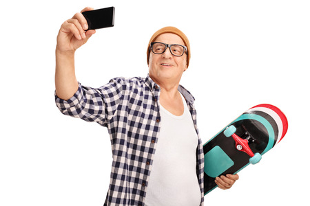 Senior skater holding a skateboard and taking a selfie with his cell phone isolated on white backgroundの写真素材