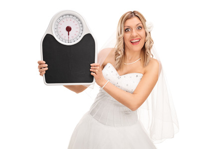Joyful bride holding a weight scale and looking at the camera isolated on white backgroundの写真素材