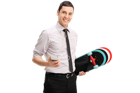 Young businessman holding a skateboard and listening to music on headphones isolated on white backgroundの写真素材