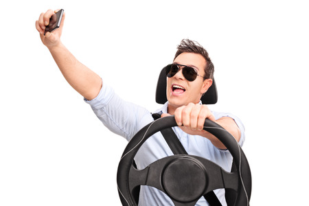 Young man driving and taking a selfie with his cell phone isolated on white background