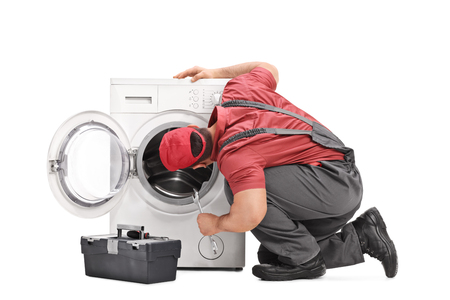 Young repairman examining a washing machine and holding a wrench isolated on white backgroundの写真素材