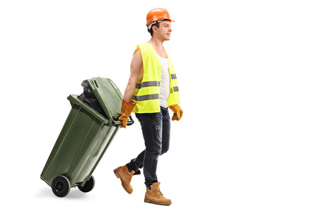 Full length portrait of a male waste collector dragging a trash can isolated on white background