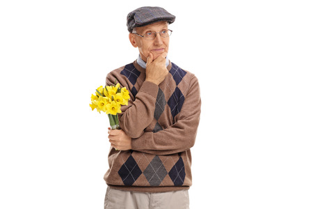 Pensive senior gentleman holding a bunch of flowers and looking in the distance isolated on white backgroundの写真素材