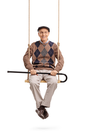 Vertical shot of a senior holding his cane and sitting on a wooden swing isolated on white backgroundの写真素材
