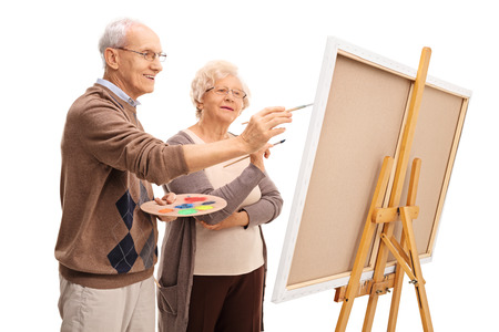 Elderly couple painting on a canvas together with paintbrushes isolated on white backgroundの写真素材
