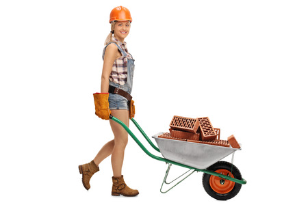 Female construction worker pushing a wheelbarrow full of bricks isolated on white backgroundの写真素材