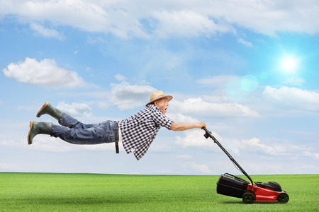Mature man being pulled by a powerful lawnmower outdoors on a beautiful sunny dayの写真素材