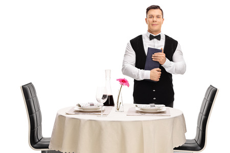 Young waiter standing next to a restaurant table and holding a menu isolated on white backgroundの写真素材