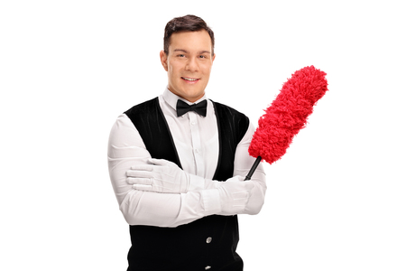 Young cheerful butler holding a duster and looking at the camera isolated on white backgroundの写真素材