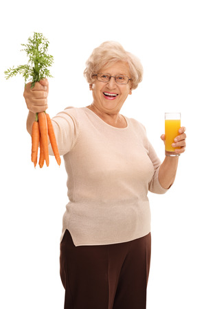 Vertical shot of a elderly woman holding a bunch of carrots and a glass of juice isolated on white backgroundの写真素材