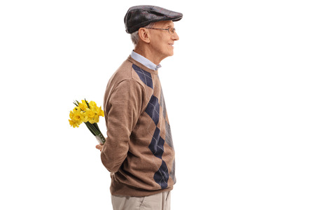 Romantic senior gentleman holding a bunch of yellow tulips behind his back isolated on white backgroundの写真素材