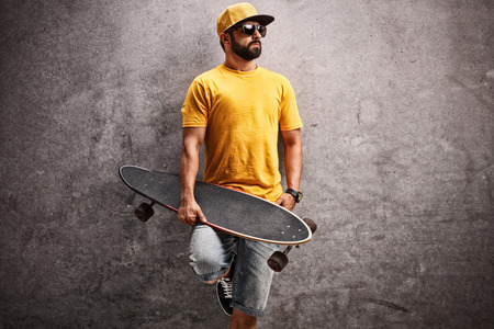 Man holding a longboard and leaning against a rusty concrete wallの写真素材