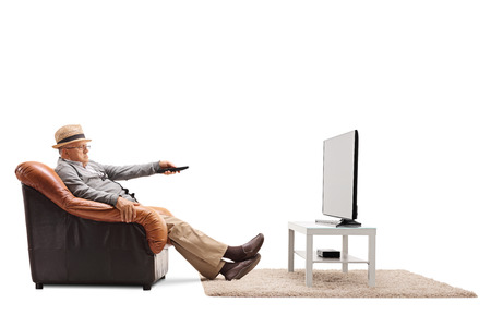 Bored senior changing channels on his TV seated on an armchair isolated on white background