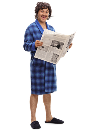Full length portrait of an excited young man in a blue bathrobe holding a newspaper isolated on a white backgroundの写真素材