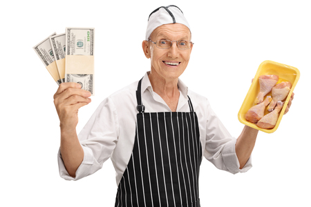 Elderly butcher holding stacks of money and chicken drums isolated on white backgroundの写真素材
