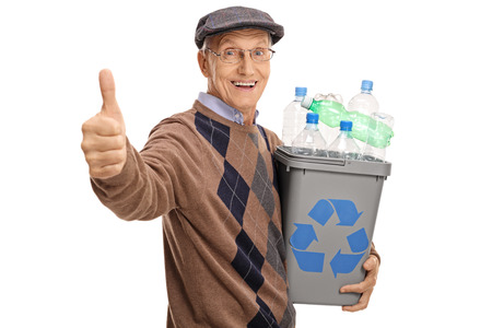 Cheerful mature man holding a recycling bin full of plastic bottles and giving a thumb up isolated on white backgroundの写真素材