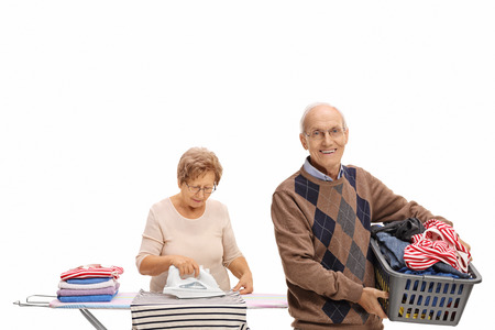 Cheerful elderly man holding a laundry basket and a mature woman ironing isolated on white backgroundの写真素材