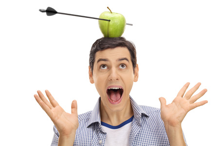Scared guy looking at an apple pierced by an arrow on his head isolated on white backgroundの写真素材