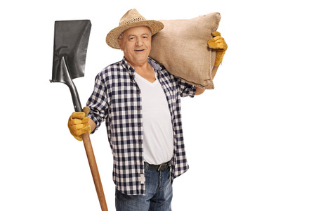 Joyful elderly farmer posing with a shovel and a burlap sack isolated on white backgroundの写真素材