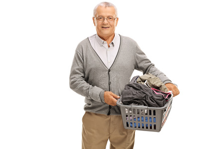 Elderly man holding a laundry basket full of clothes isolated on white backgroundの写真素材