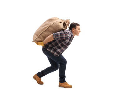 Full length profile shot of a male agricultural worker carrying a burlap sack on his back isolated on white backgroundの写真素材