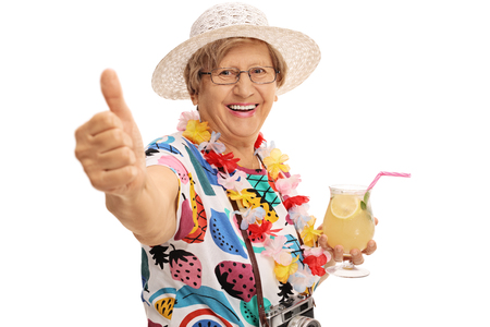 Cheerful mature tourist holding a cocktail and making a thumb up gesture isolated on white backgroundの写真素材