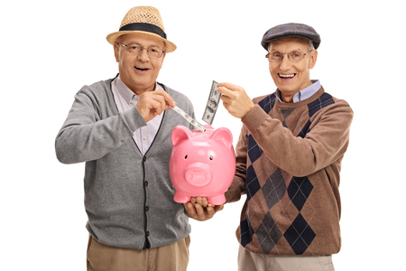 Seniors putting money in a piggybank and looking at the camera isolated on white backgroundの写真素材