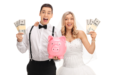 Happy newlywed couple with a piggybank and money bundles isolated on white backgroundの写真素材
