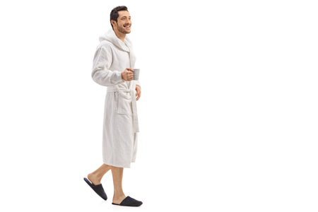 Full length portrait of a young man in a bathrobe holding a cup and walking isolated on white backgroundの写真素材