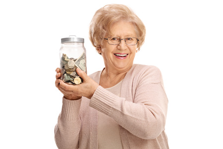 Happy mature lady holding a jar filled with money isolated on white backgroundの写真素材