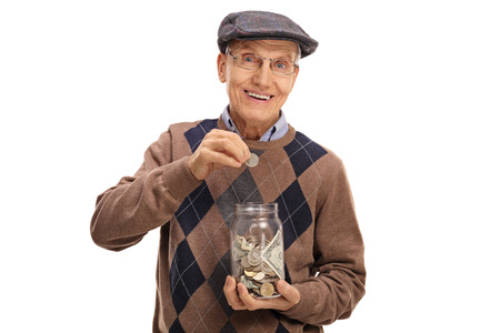 Elderly man putting a coin into a jar with money isolated on white backgroundの写真素材