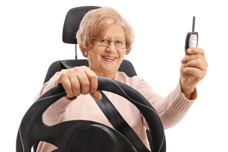 Mature woman sitting in a car seat and holding a car key isolated on white backgroundの写真素材