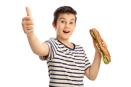Joyful young boy holding a sandwich and giving a thumb up isolated on white backgroundの写真素材