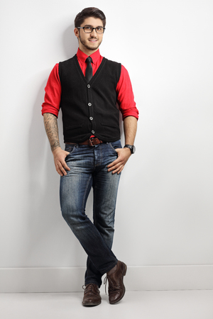 Full length portrait of a tattooed guy leaning against a white wallの写真素材