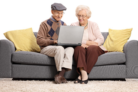 Seniors sitting on a sofa and using a laptop isolated on white backgroundの写真素材