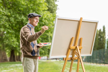 Elderly man painting on a canvas in the parkの写真素材
