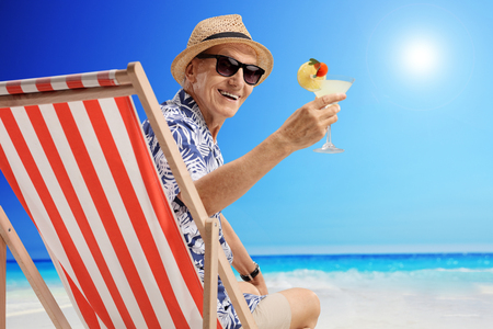 Mature man with a cocktail sitting in a deck chair on a beachの写真素材